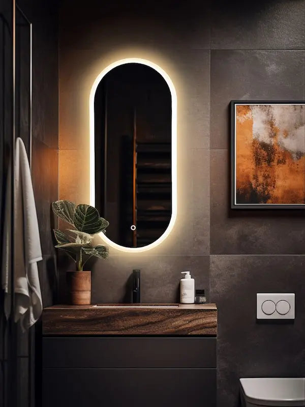 Bathroom with a illuminated oval mirror, plant, and wall art.