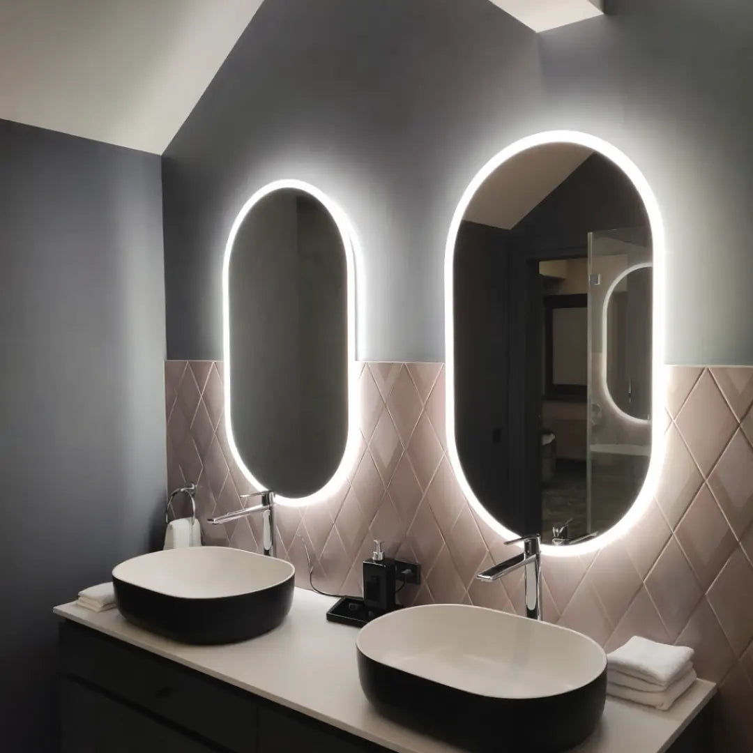Bathroom vanity with two black sinks and illuminated mirrors.