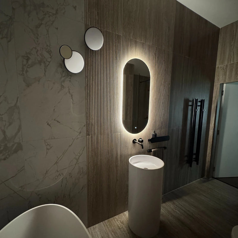 Modern bathroom with a illuminated oval mirror, sink, and towel rack.